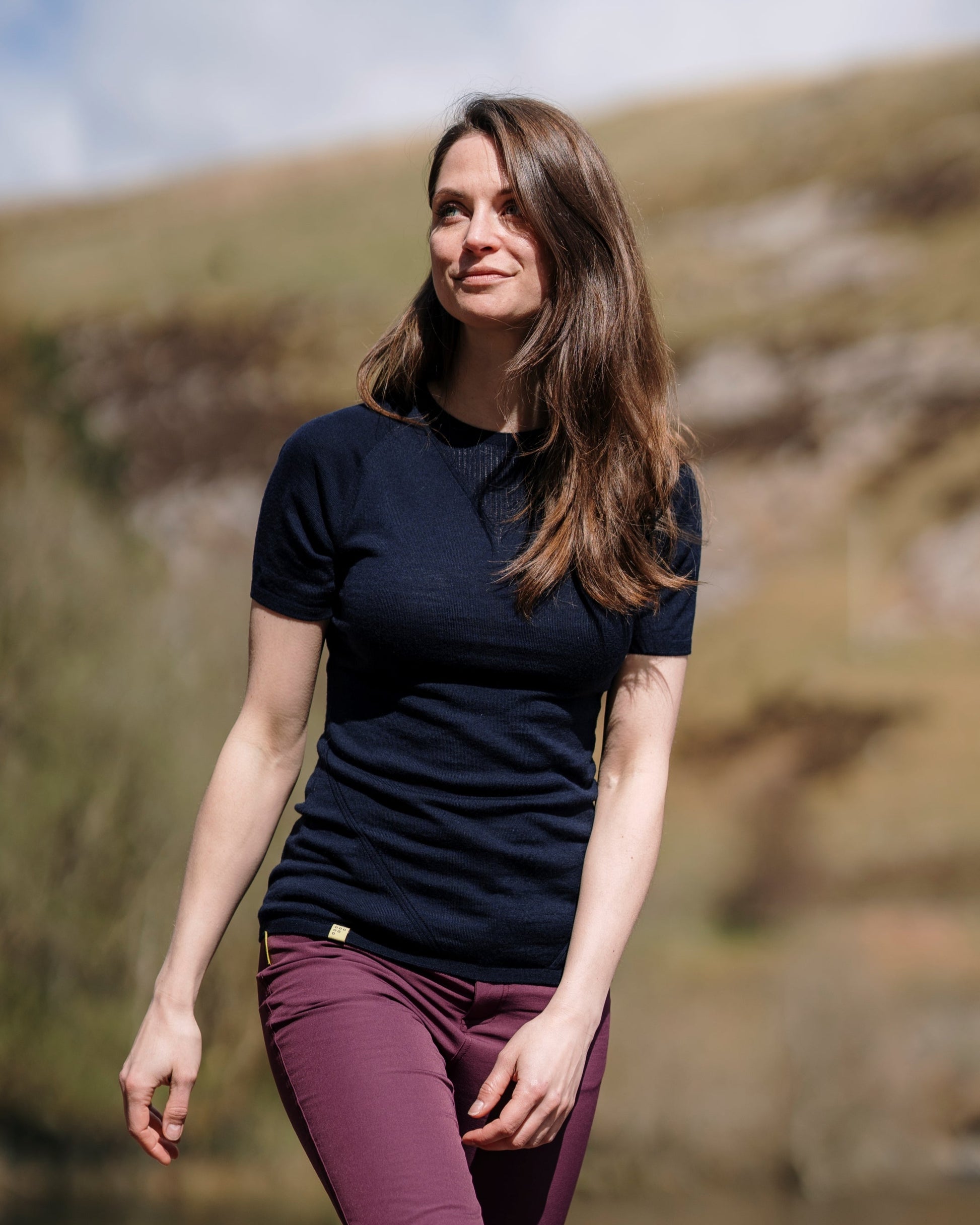 A woman standing outdoors wearing a navy Merino Wool t-shirt and Wine outdoor trousers.