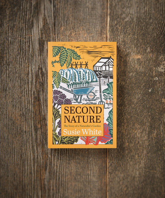 A book titled 'Second Nature' by Susie White, featuring a garden and nature-themed design on its cover, placed on a wooden surface.