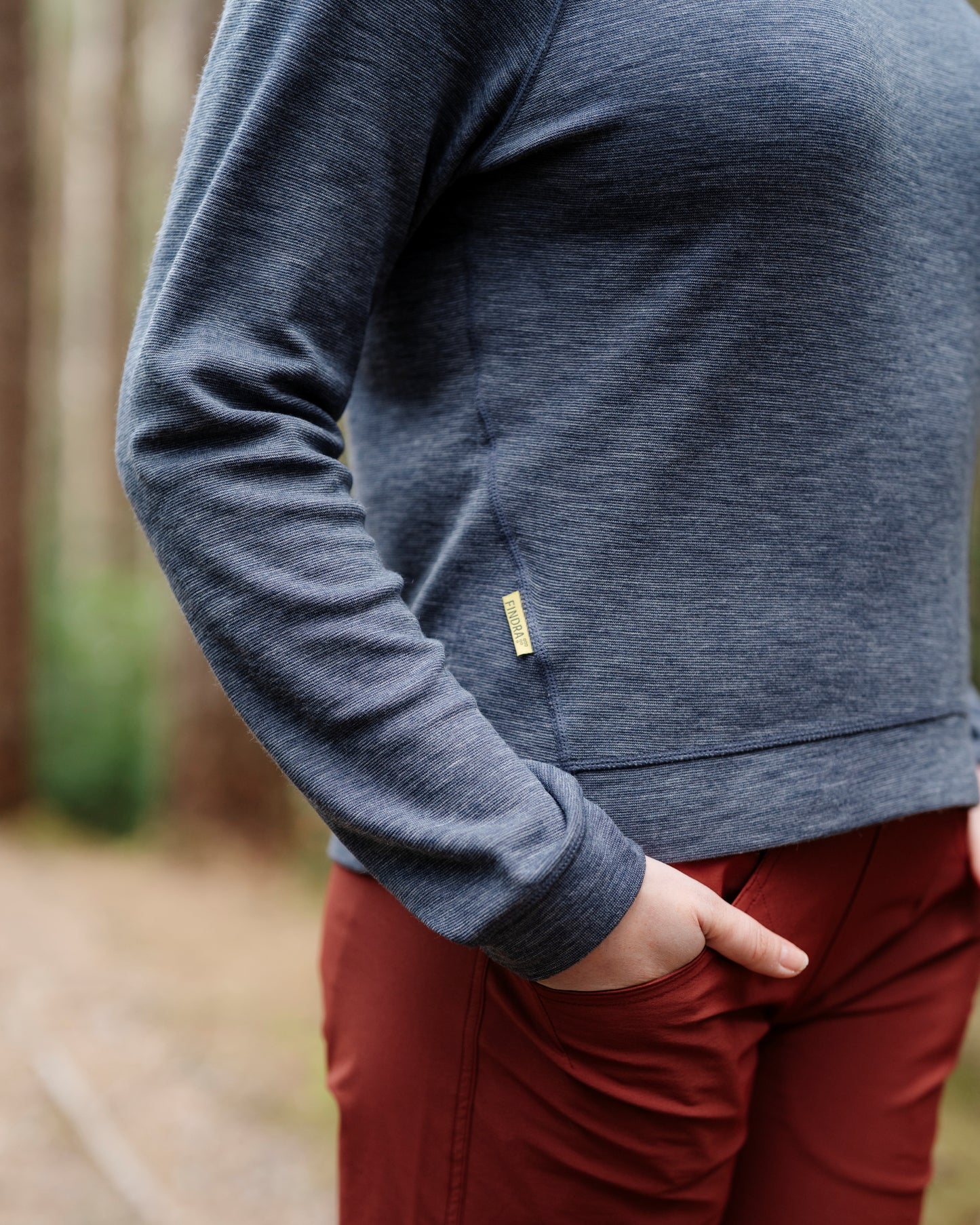 Person wearing a blue long-sleeve shirt with a yellow label in a forest setting