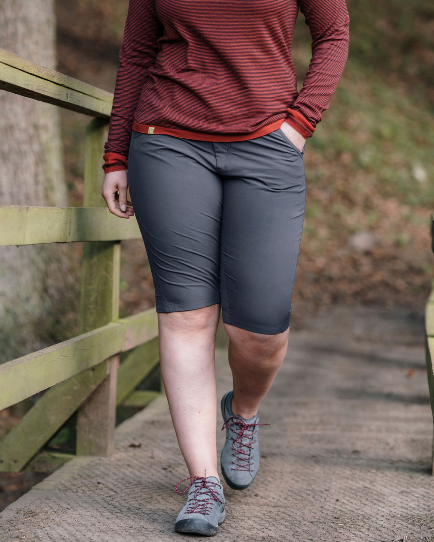 A person stands in a natural outdoor setting wearing green trail shorts and gray hiking shoes.