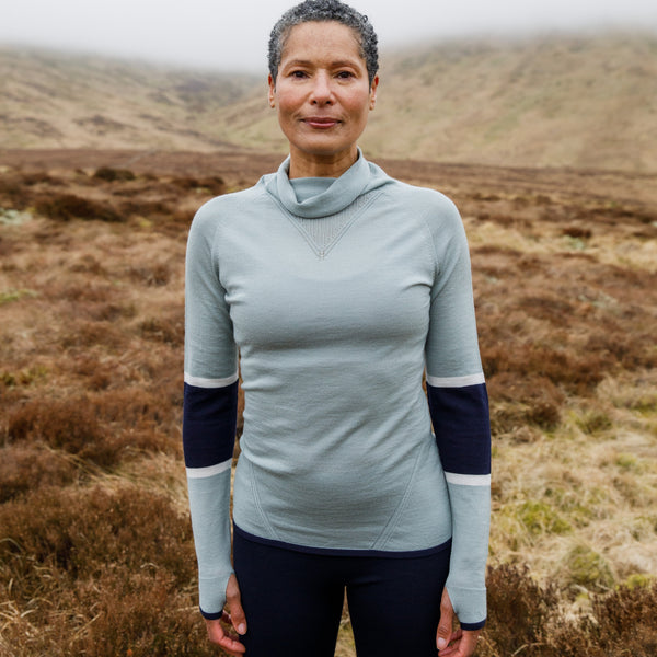 Woman on a hillside in Autumn with a Merino Wool Hoodie on pulling the hood up
