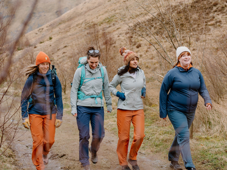 Four women hiking on a trail with mountains in the background wearing the FINDRA Technical Performance Collection
