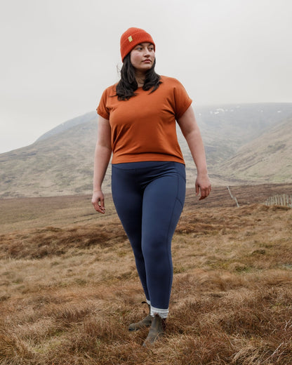 Person wearing an orange shirt and blue leggings standing in a field with mountains in the background