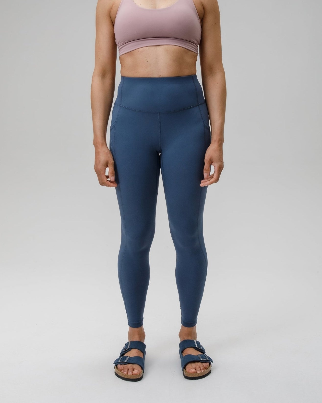 Woman wearing a pink sports bra and blue leggings on a gray background