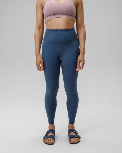 Woman wearing a pink sports bra and blue leggings on a gray background