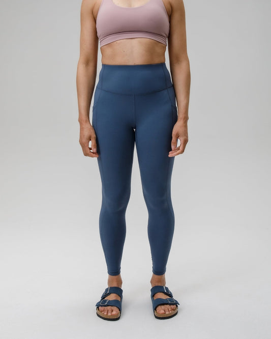 Woman wearing a pink sports bra and blue leggings on a gray background