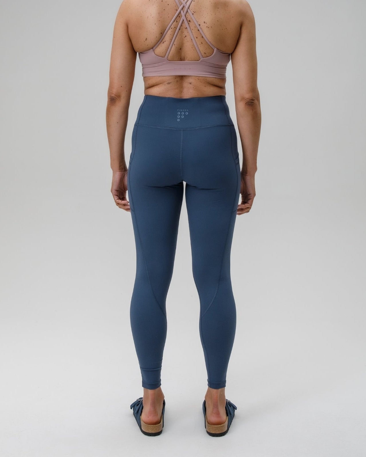 Person wearing a sports bra and blue leggings on a plain background
