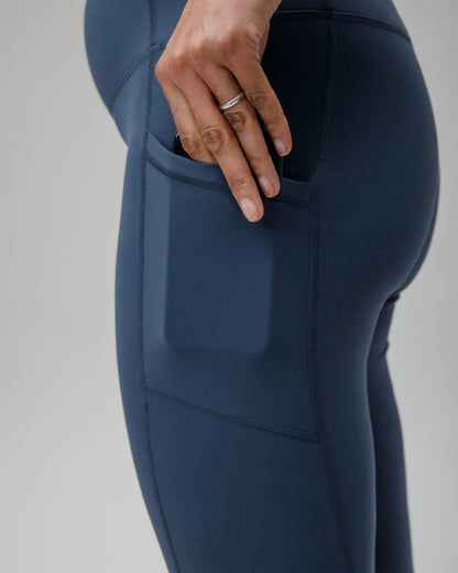 Navy blue athletic leggings with a pocket on a gray background