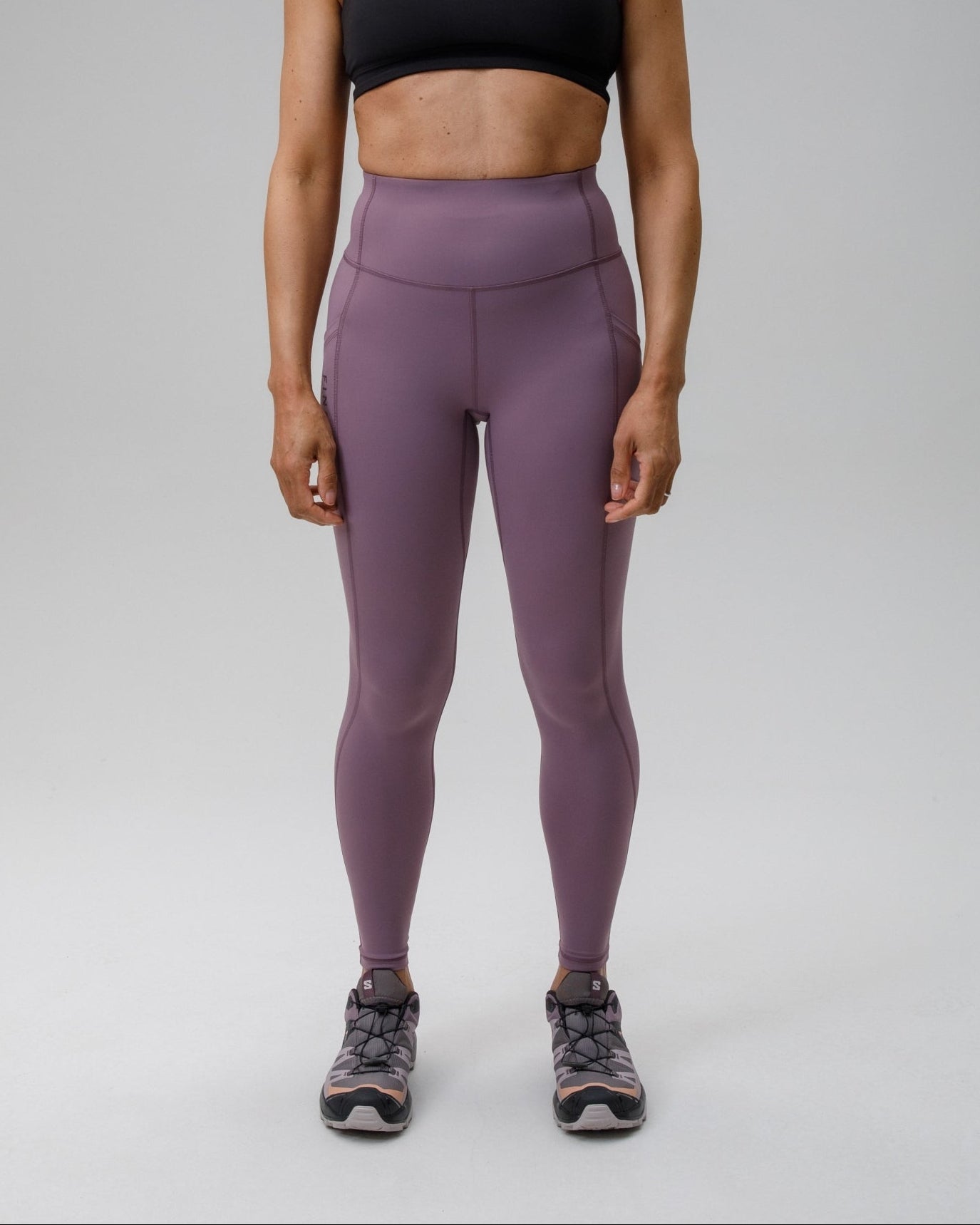 Woman wearing a black sports bra and purple FINDRA performance leggings on a grey background