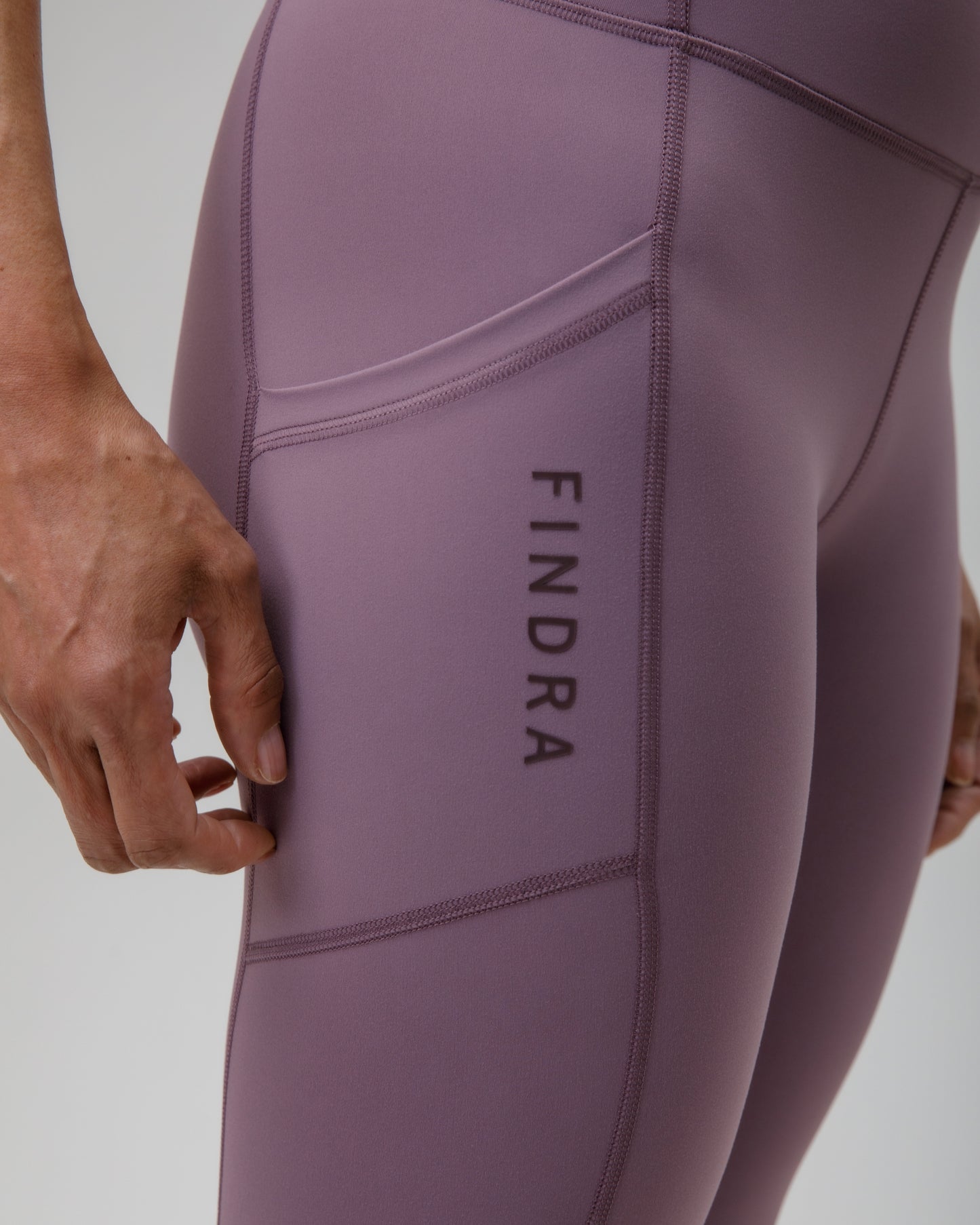 Close-up of a person wearing purple leggings with 'FINDRA' branding on a light gray background