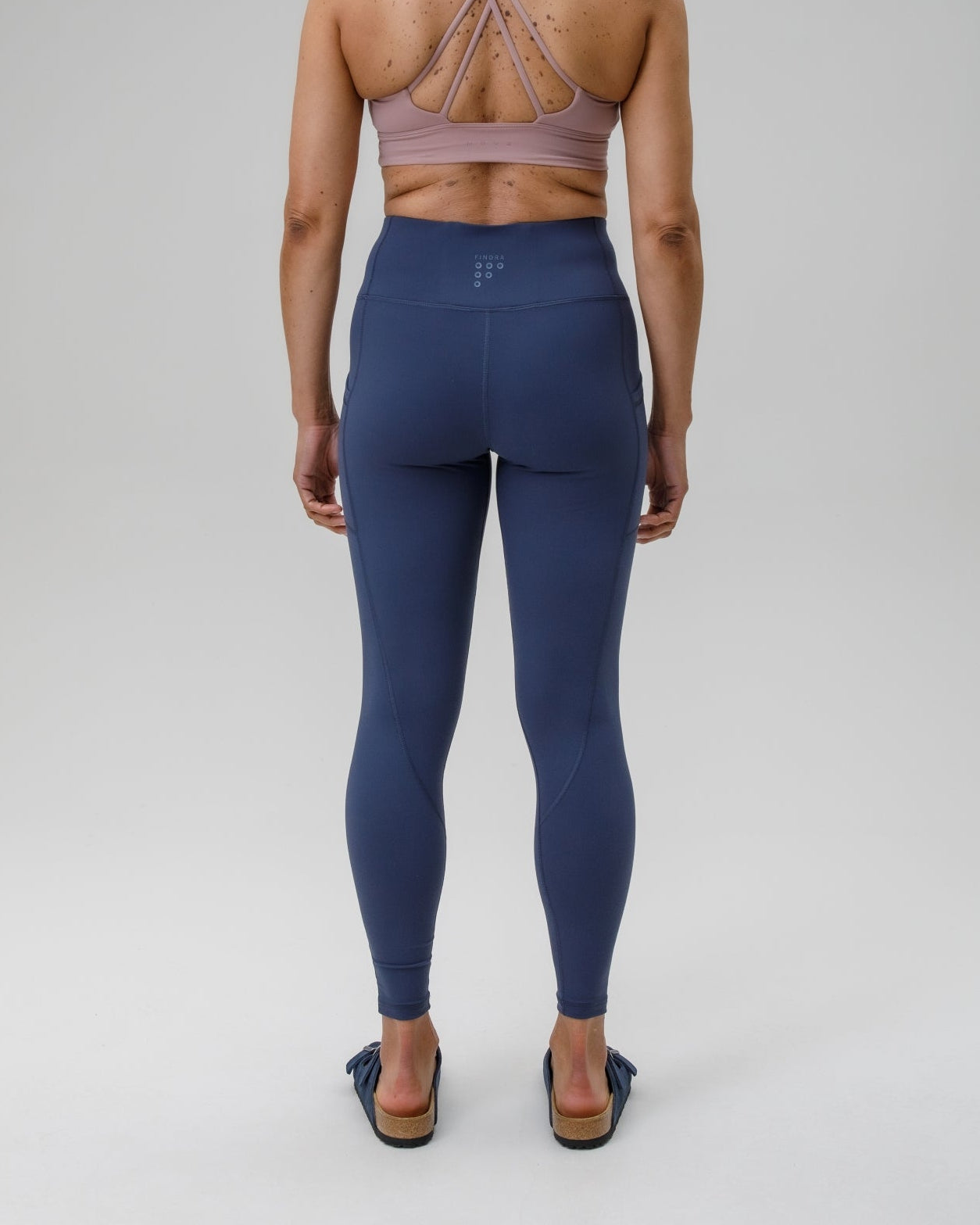 Person wearing a sports bra and blue performance leggings on a gray background