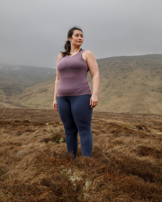 Woman standing in a field with mountains in the background wearing a merino wool vest