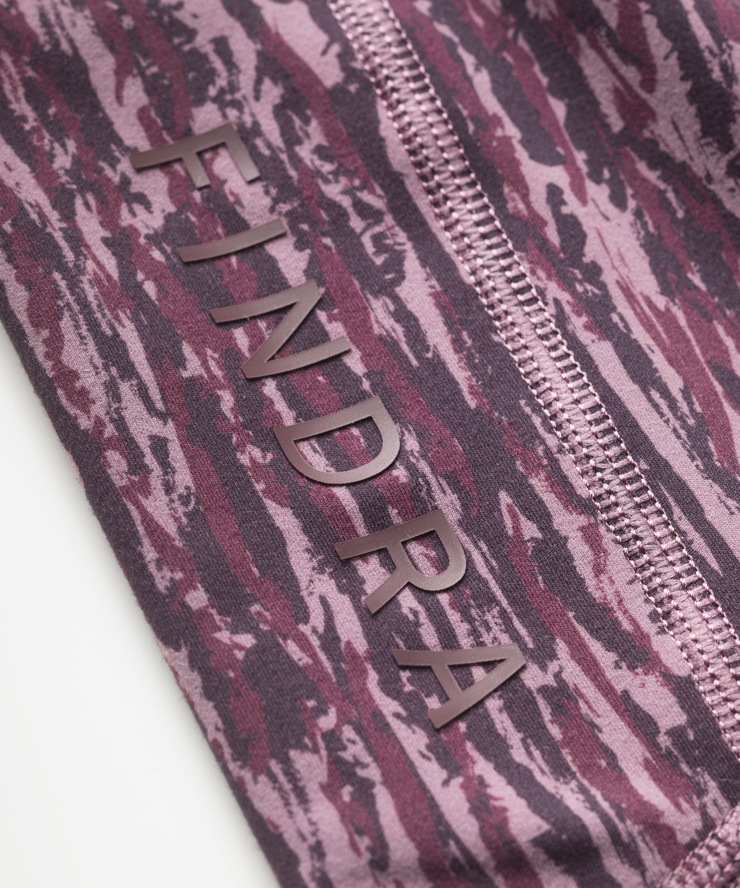 Close-up of purple patterned technical leggings with flatlocked seams and 'FINDRA' branding.