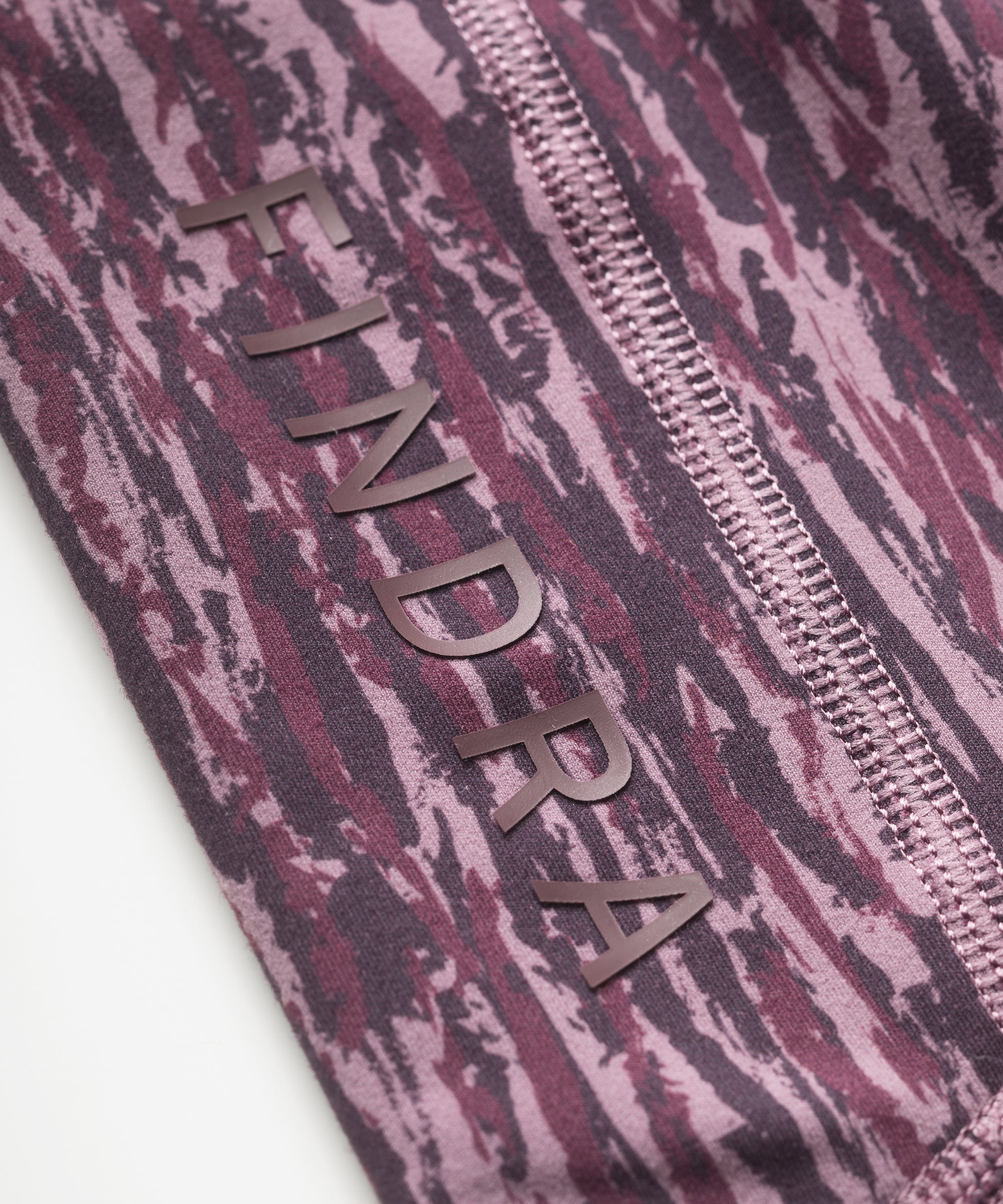Close-up of purple patterned technical leggings with flatlocked seams and 'FINDRA' branding.