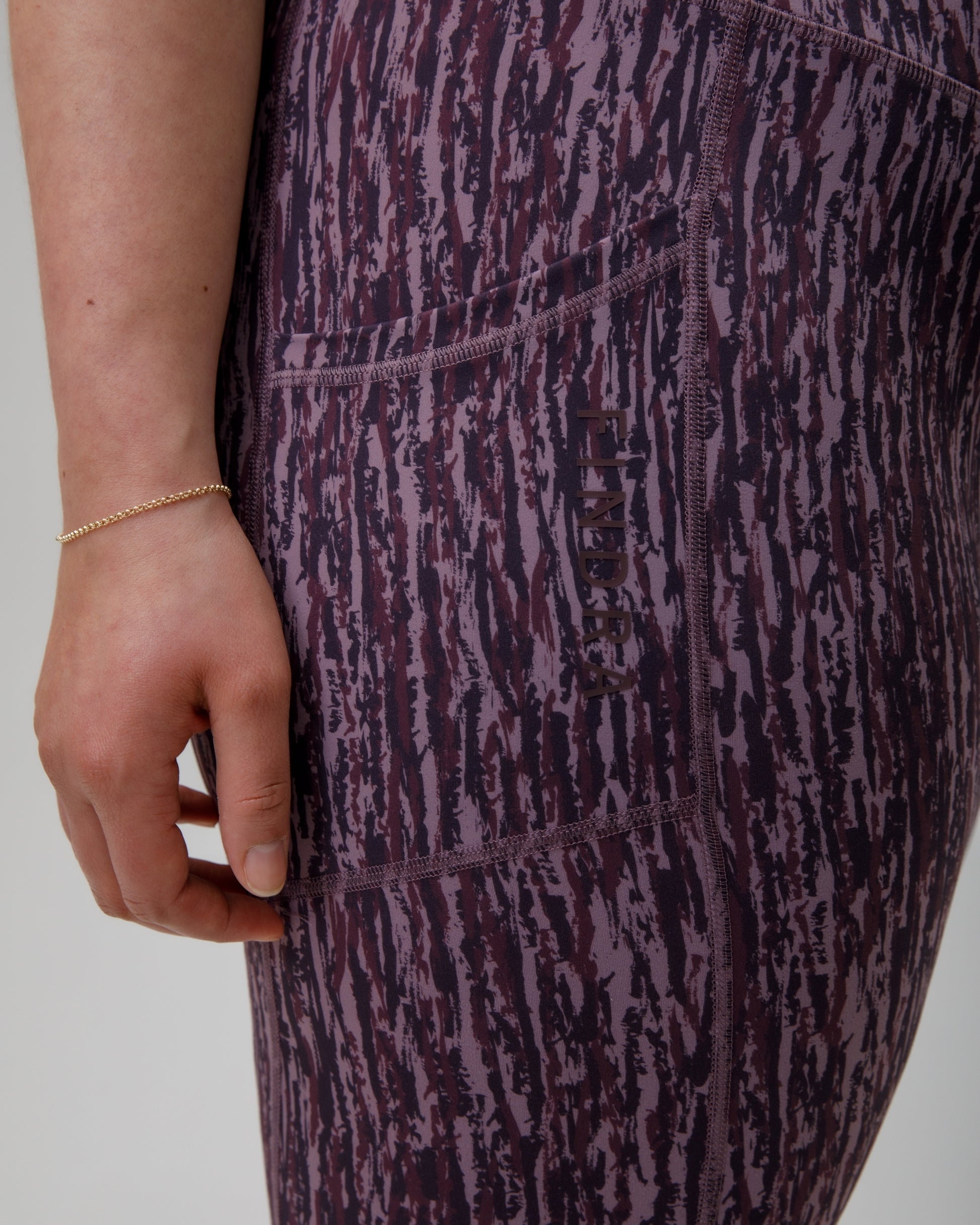Close-up of a person wearing purple patterned technical leggings with a hand visible.