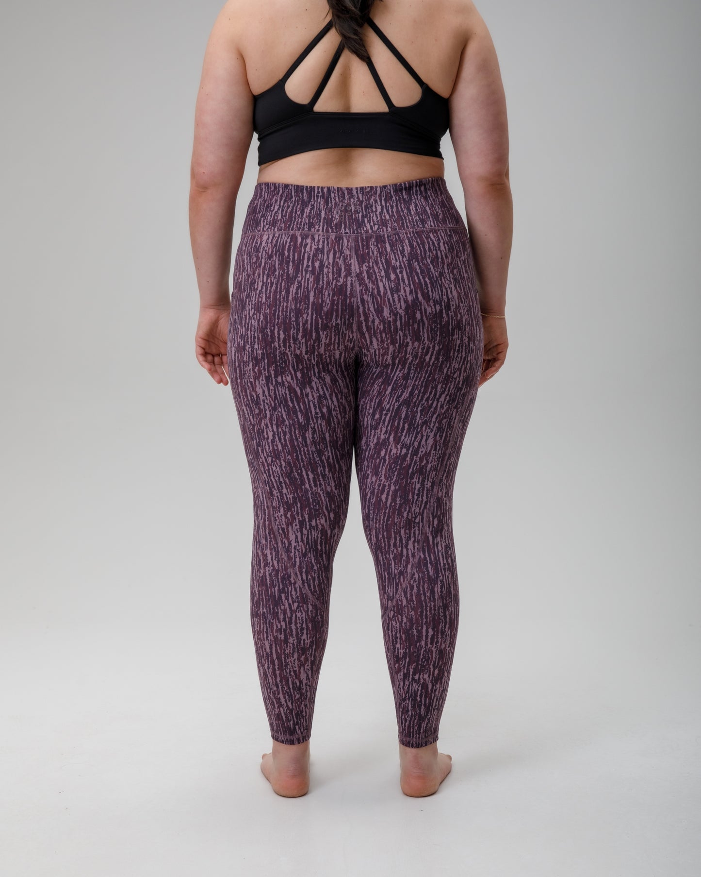 Person wearing purple patterned technical leggings and black sports bra on a gray background