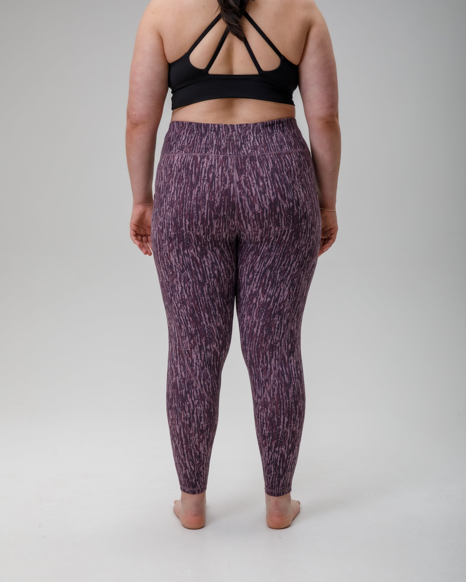 Person wearing purple patterned technical leggings and black sports bra on a gray background