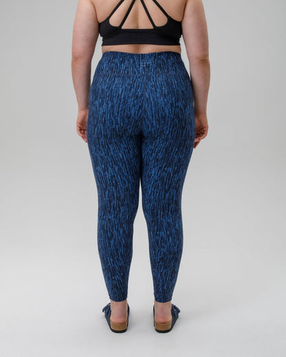 Person wearing blue patterned leggings and black strappy top on a gray background