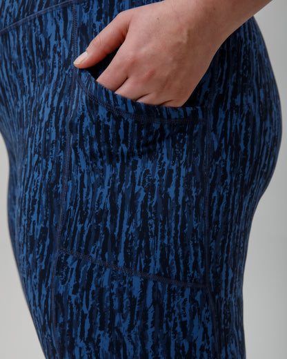 Blue patterned leggings with a handshowing the thigh pocket on a gray background