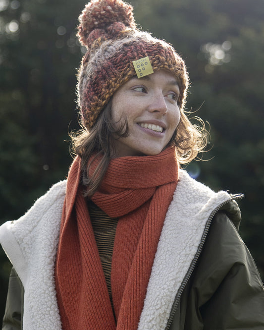 Woman wearing an autumn coloured merino wool knitted hat and scarf outdoors with trees in the background