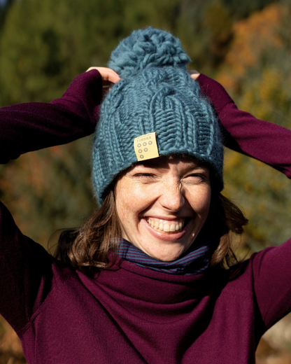 Woman wearing a blue FINDRA  knitted Bobble Hat with a yellow tag in the outdoors in Autumn