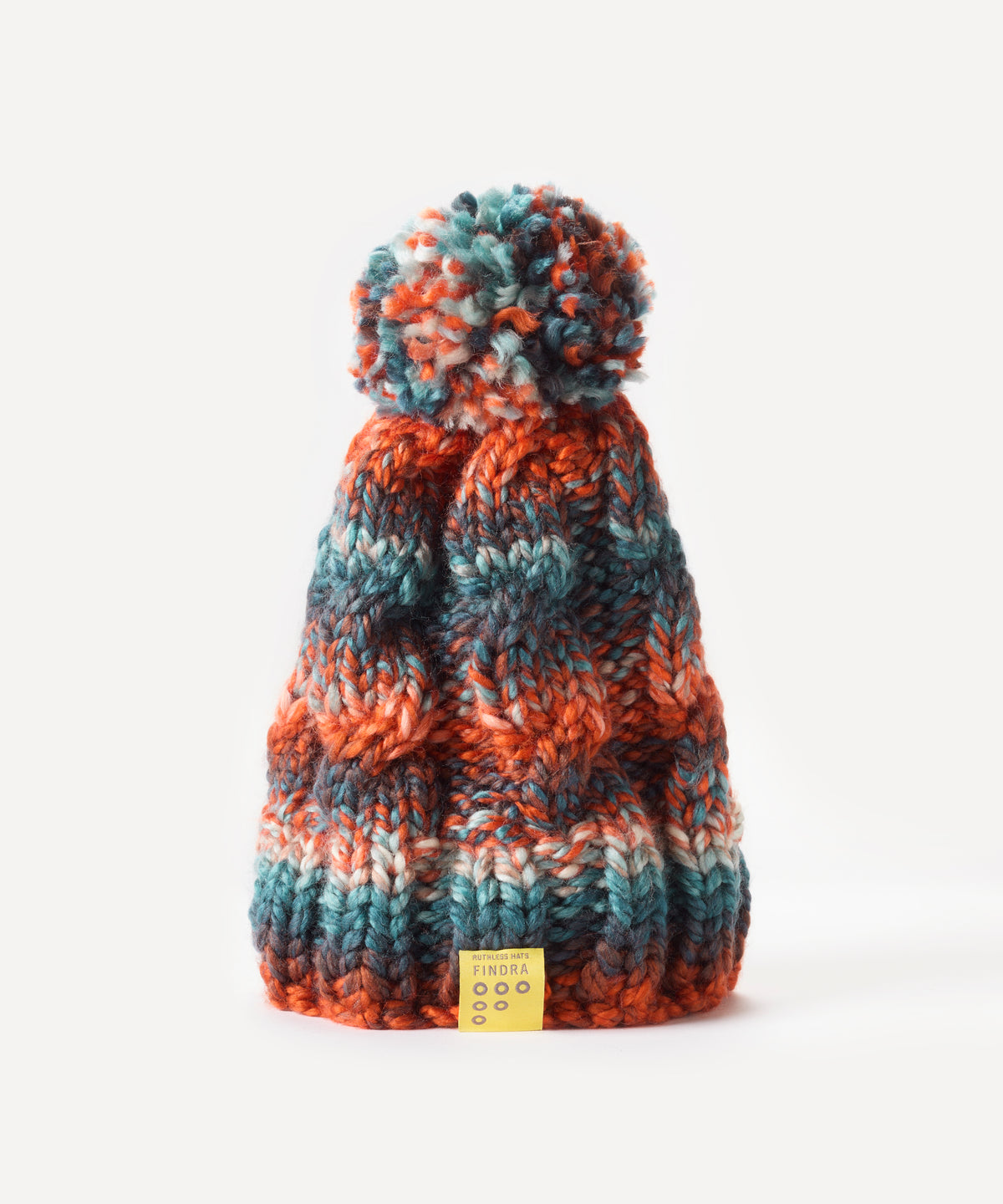 A chunky knit bobble hat with a matching pom-pom, featuring horizontal stripes of rust orange, teal blue, and cream. A small yellow brand tag is attached at the bottom, set against a clean white background.
