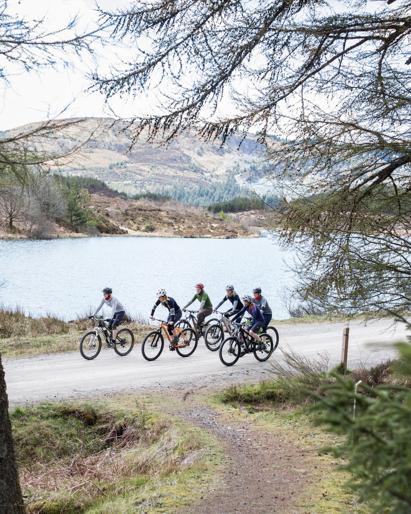 A group of women cyclists on a trail in Scotland by a loch wearing FINDRA mid and base layers. 
