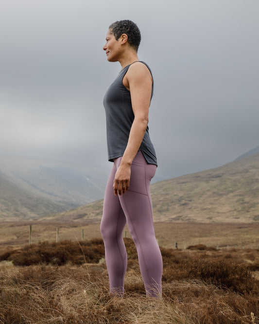 Person standing in a field wearing a FINDRA technical vest and leggings with mountains in the background