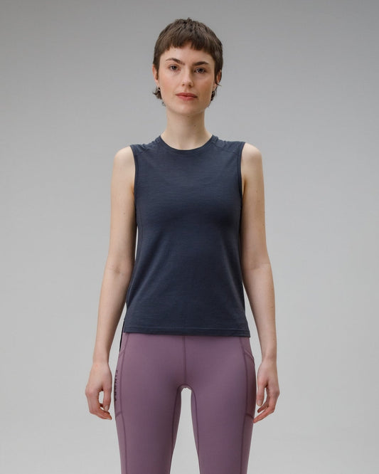 Person wearing a charcoal vest top sleeveless top and purple leggings on a gray background