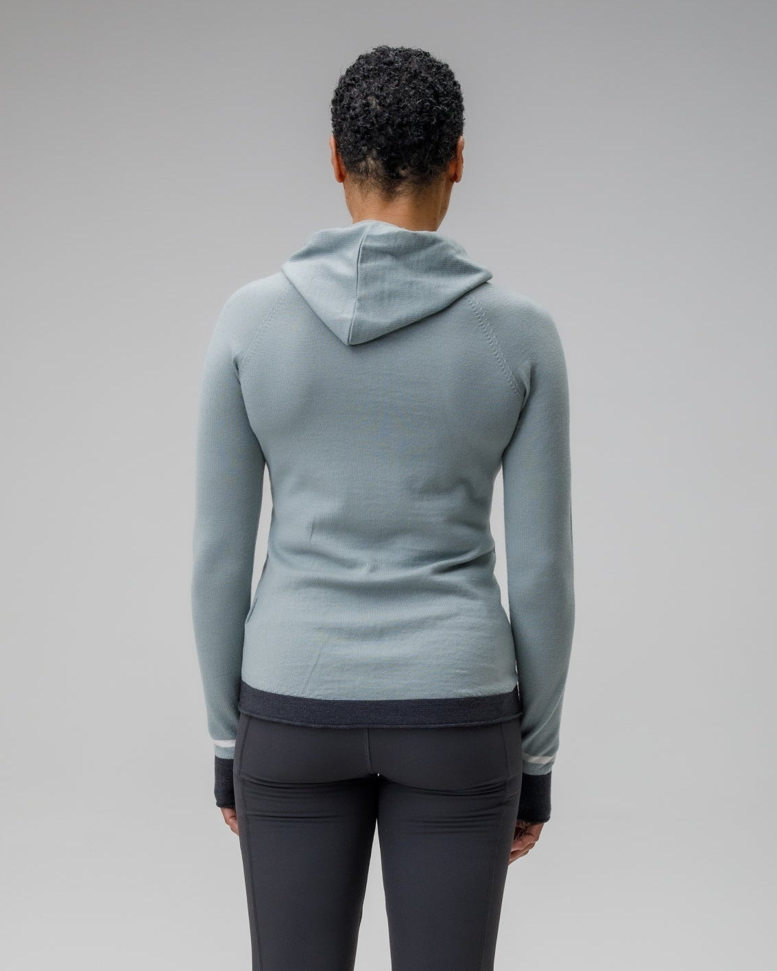 Person showing the back of a light blue grey hoodie and dark gray leggings on a plain background