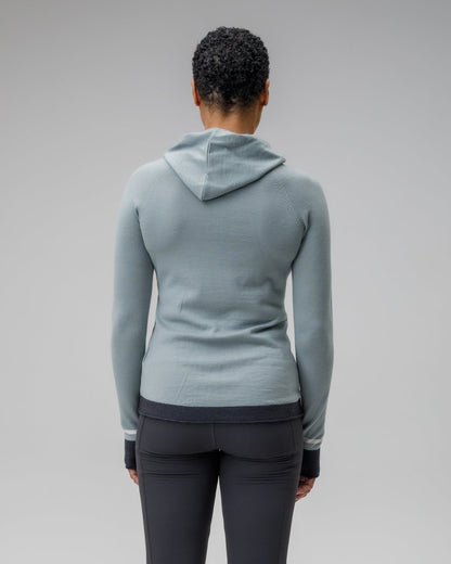Person showing the back of a light blue grey hoodie and dark gray leggings on a plain background