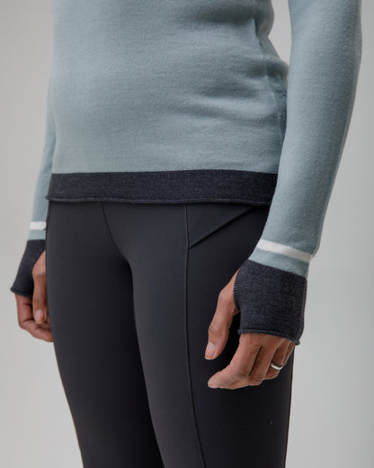 Person wearing a light blue grey Merino top with dark cuffs and white stripes, paired with black pants on a neutral background.