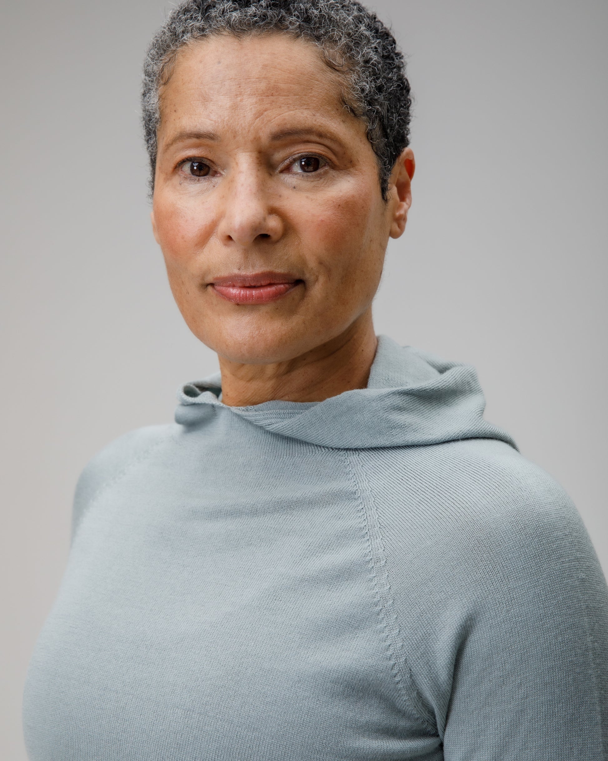 Woman wearing a light blue Merino wool hooded top against a plain background