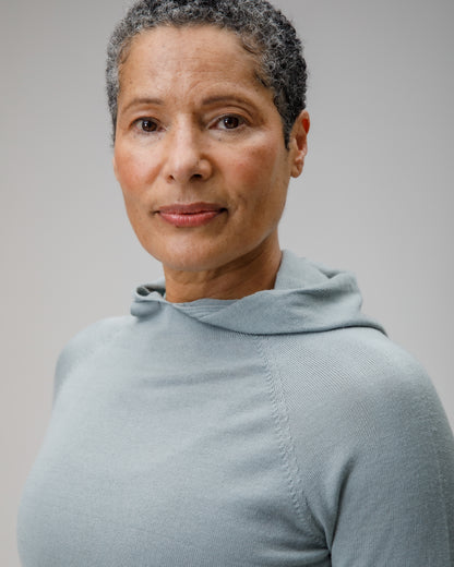 Woman wearing a light blue Merino wool hooded top against a plain background