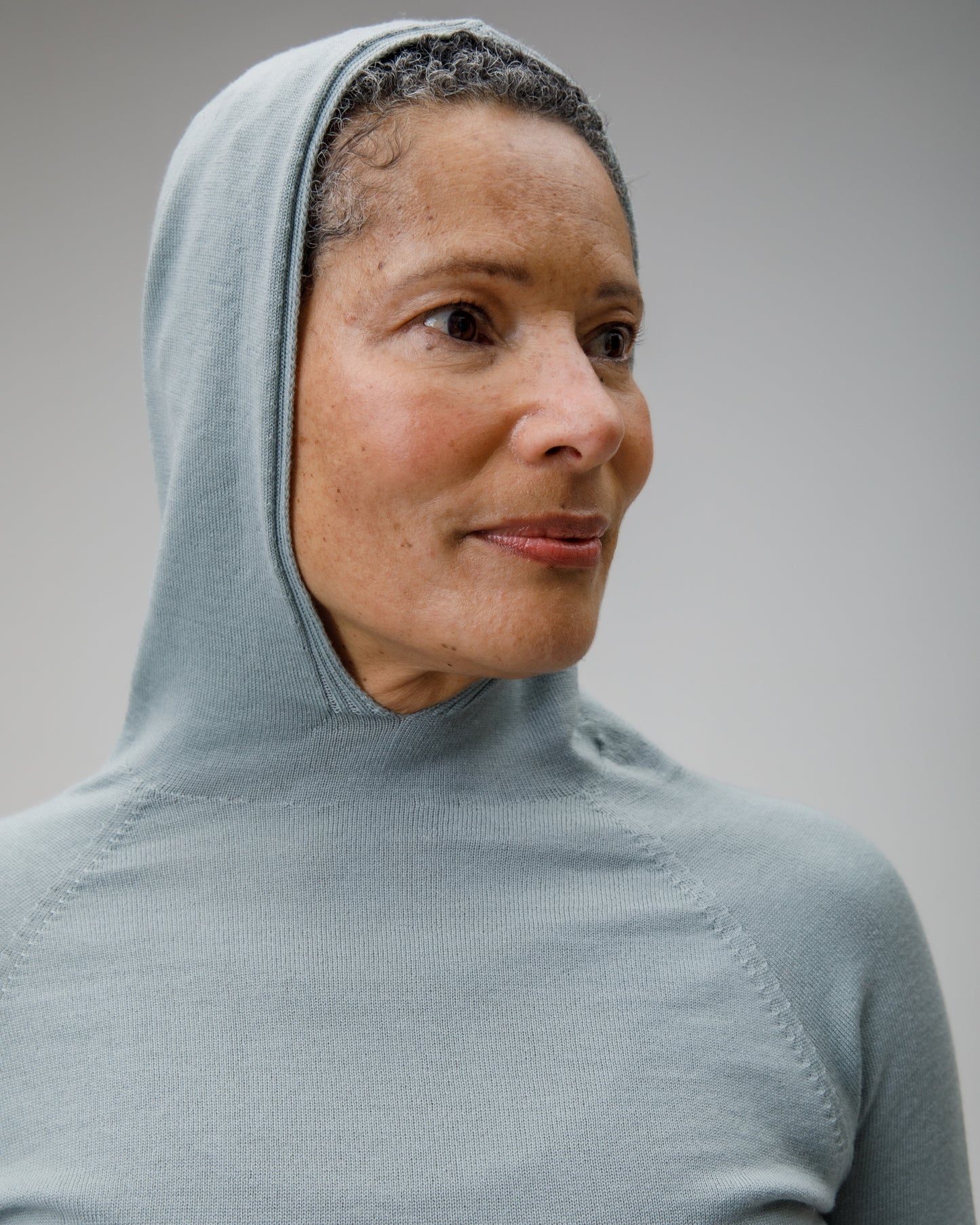 Person wearing a light grey blue Merino hooded garment against a neutral background