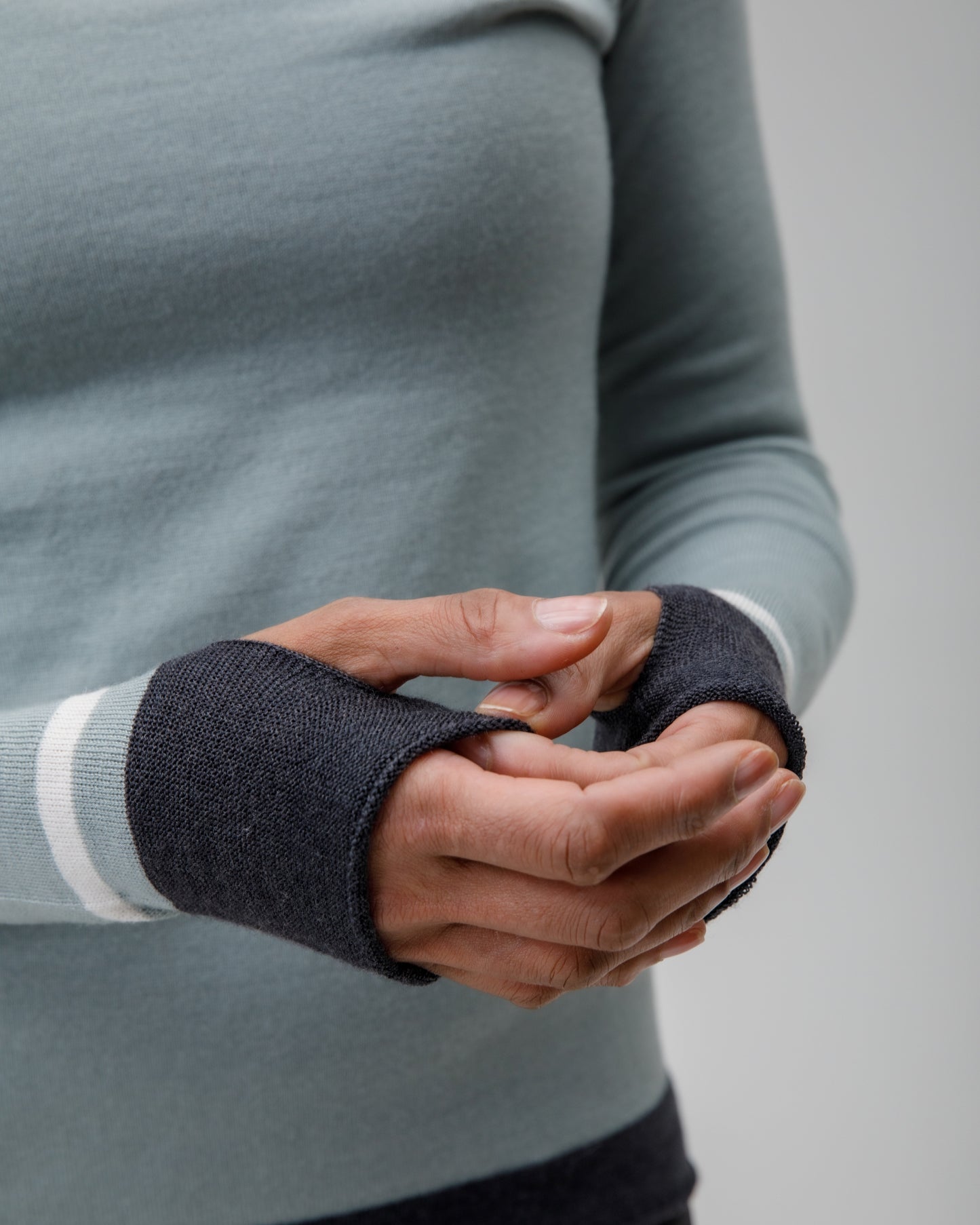Person wearing a light blue grey Merino top with dark wrist thumbholes on a plain background