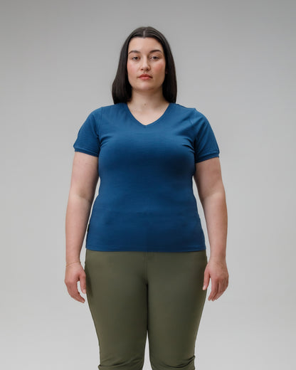 Woman wearing a blue t-shirt and green pants against a gray background