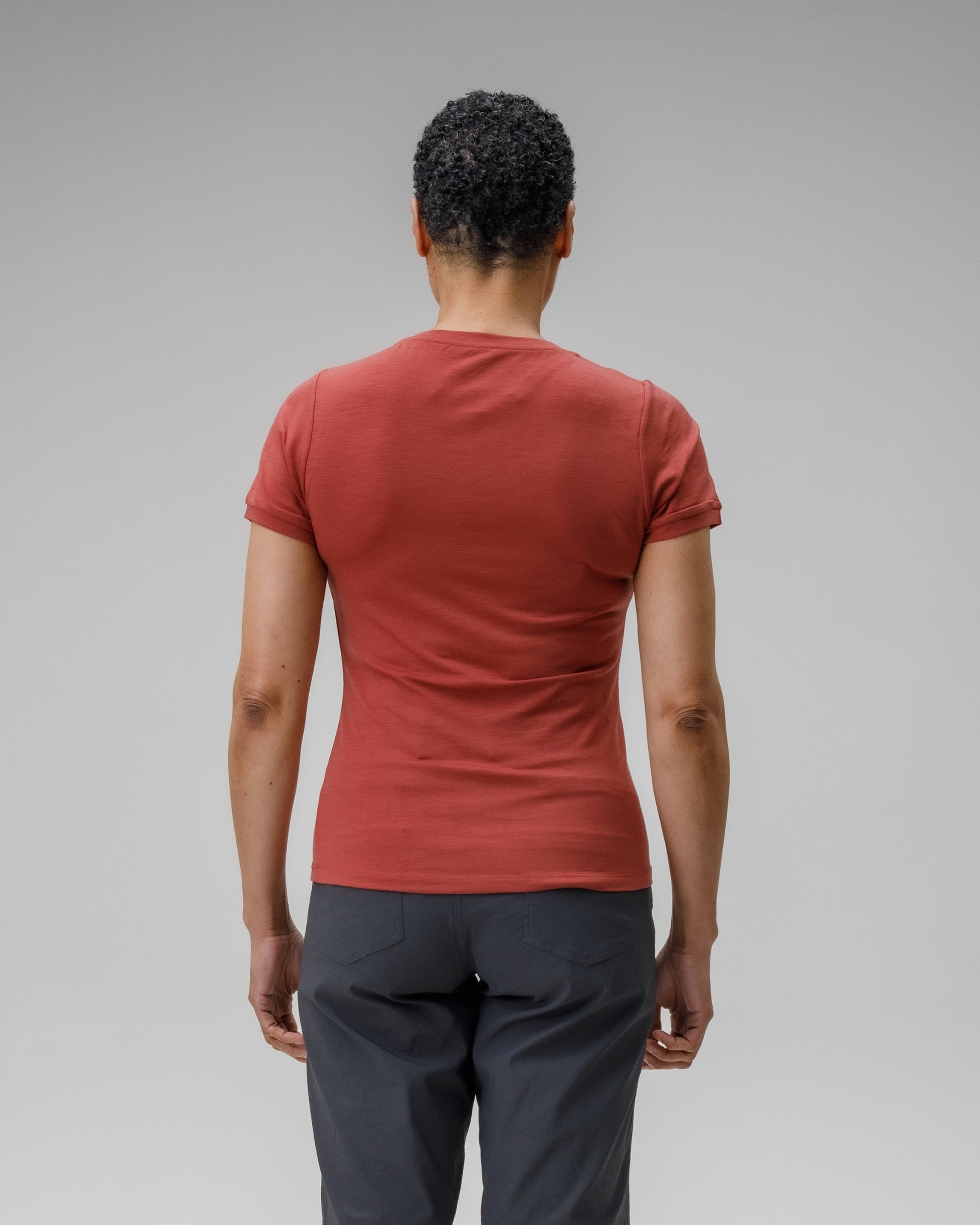 Person wearing a red t-shirt and dark pants on a gray background