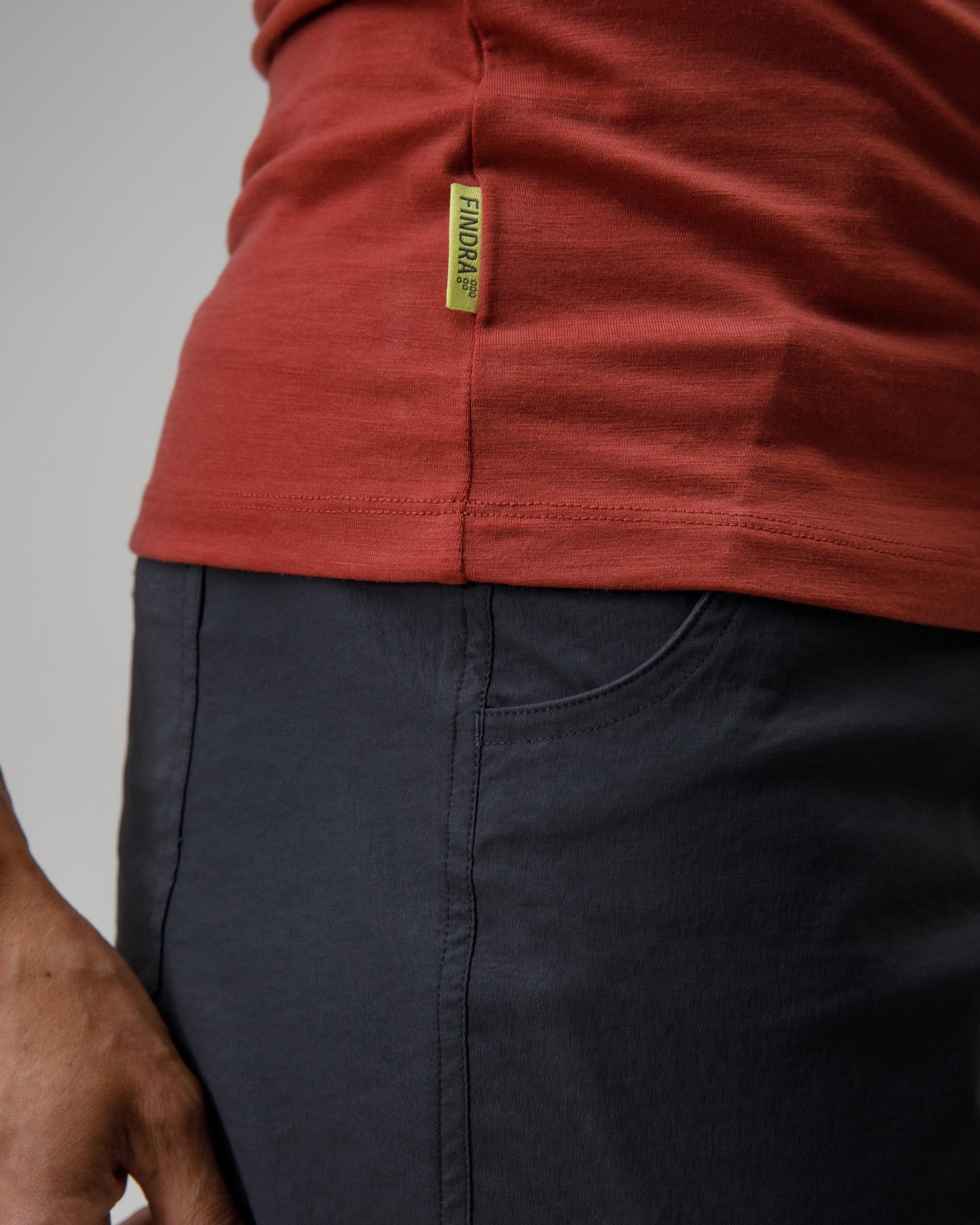 Person wearing a red shirt with a visible brand label and dark pants on a plain background