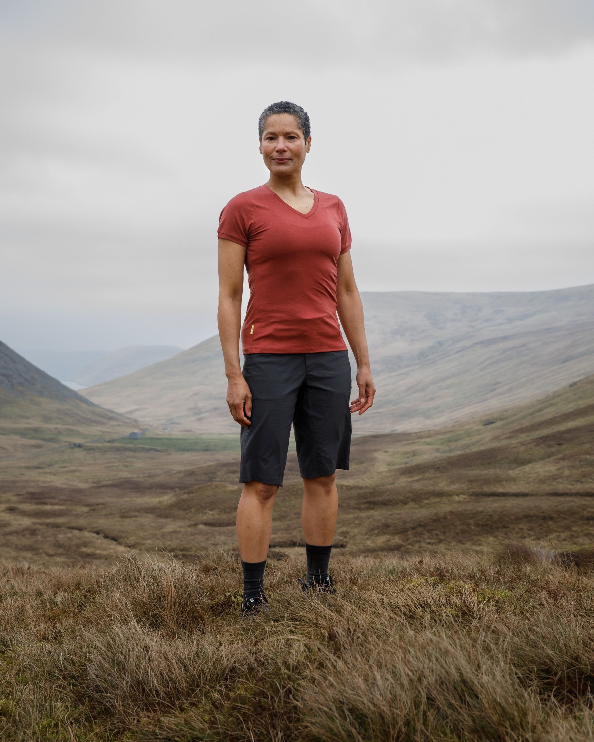 Person standing in a grassy field with mountains in the background wearing a "FINDRA" red t-shirt and shorts