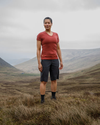 Person standing in a grassy field with mountains in the background wearing a "FINDRA" red t-shirt and shorts