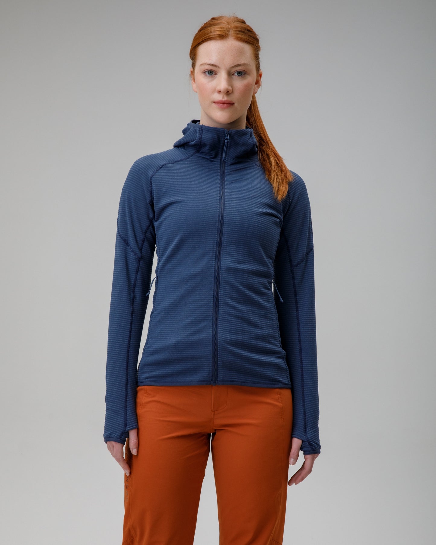 Woman wearing a blue jacket and orange pants on a gray background