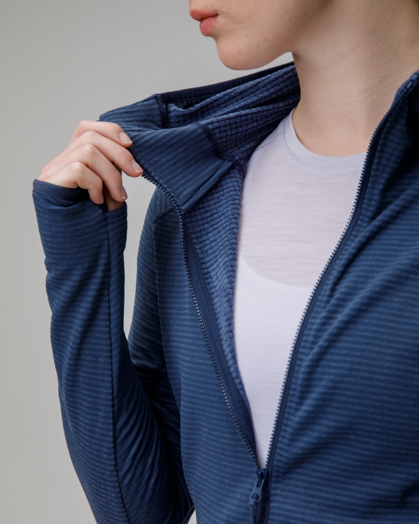 Person wearing a blue ribbed sweater over a white shirt on a gray background