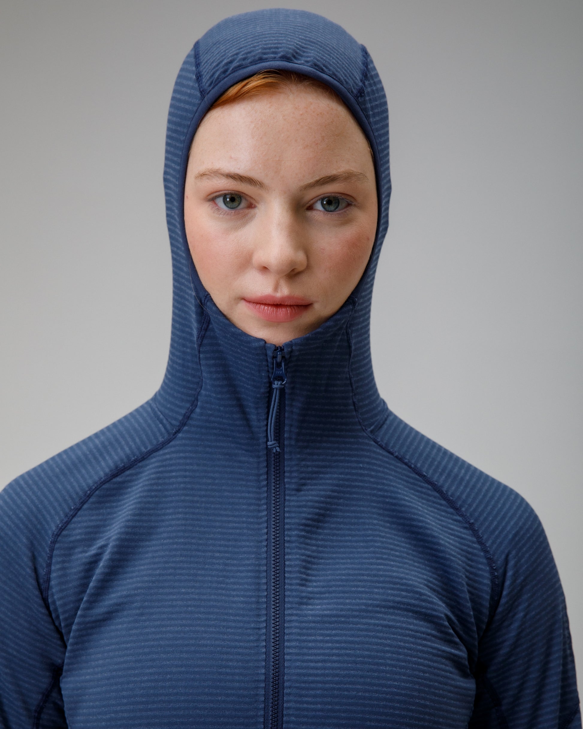 Person wearing a blue hooded jacket against a gray background
