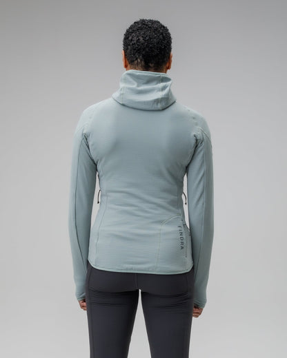 Woman wearing a light blue jacket and dark gray leggings on a plain background