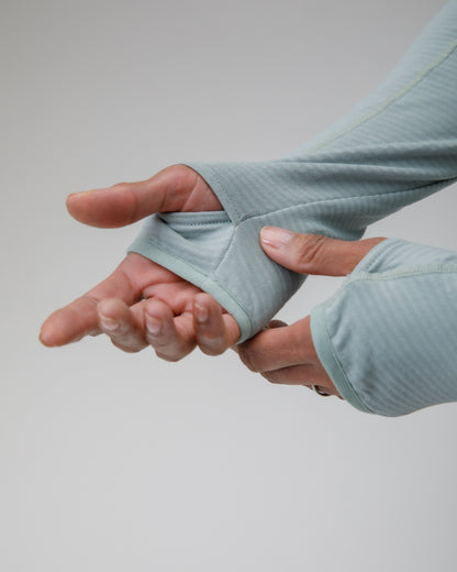 Person wearing a light blue top with thumbholes on the sleeve on a plain background