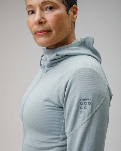 Person wearing a light gray hoodie with brand logo on sleeve against a plain background