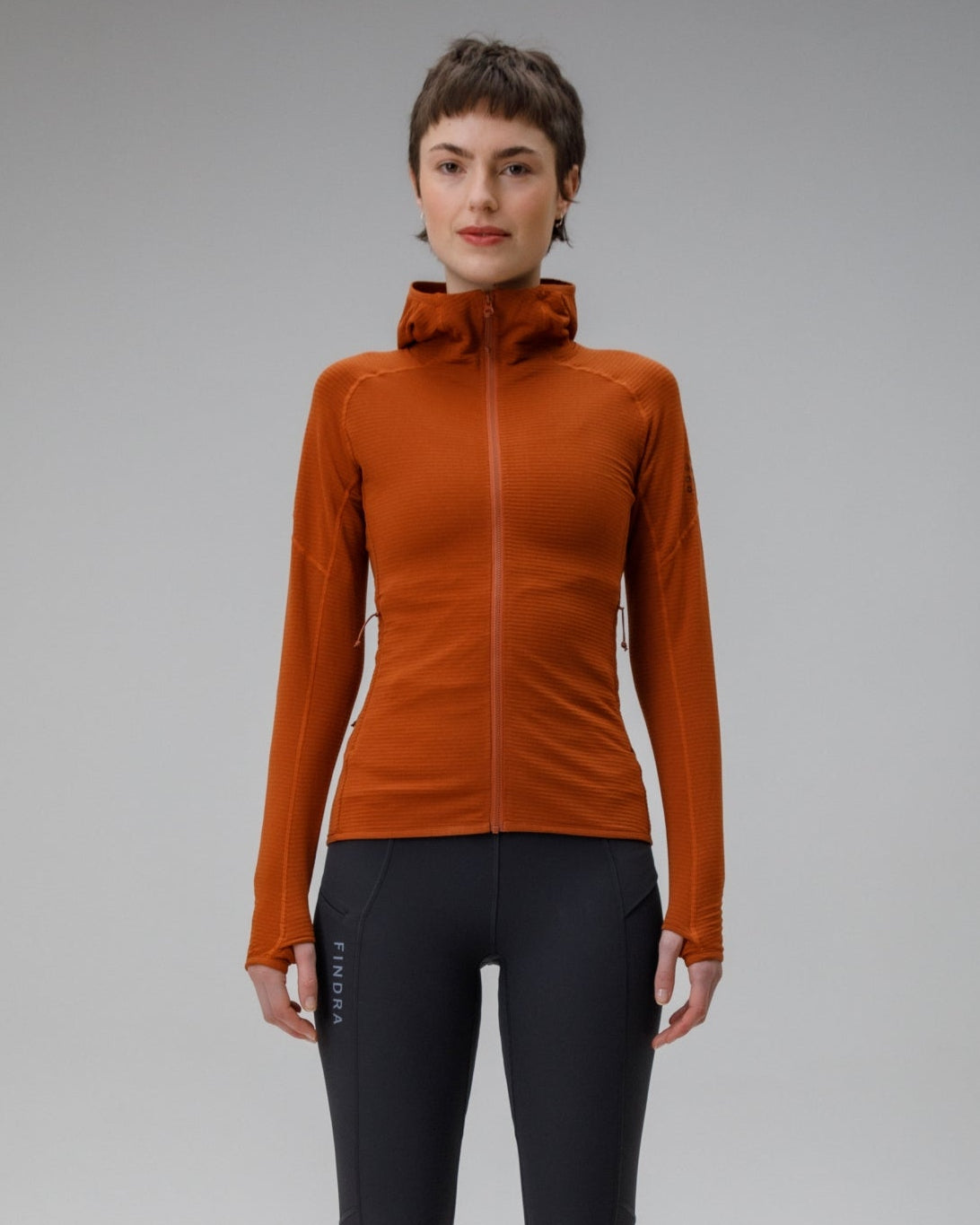 Person wearing an orange jacket and black leggings on a gray background