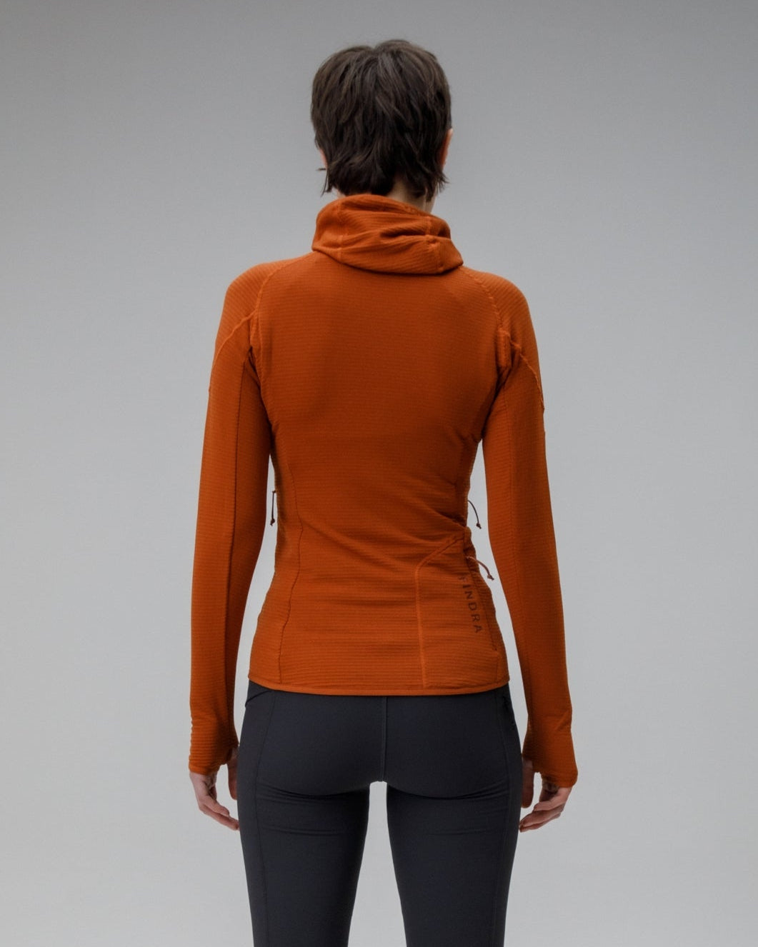 Person wearing a rust-colored long-sleeve top and black leggings on a gray background