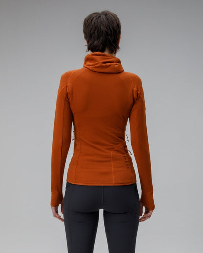 Person wearing a rust-colored long-sleeve top and black leggings on a gray background